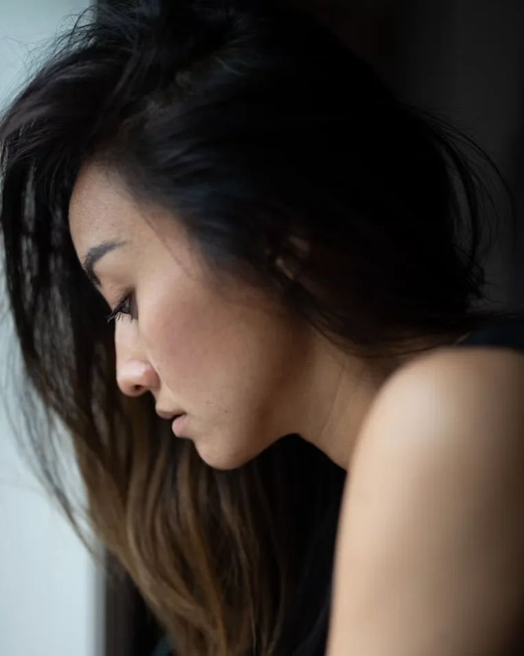 A woman looking down thoughtfully, illustrating the emotional side of living with PMOS